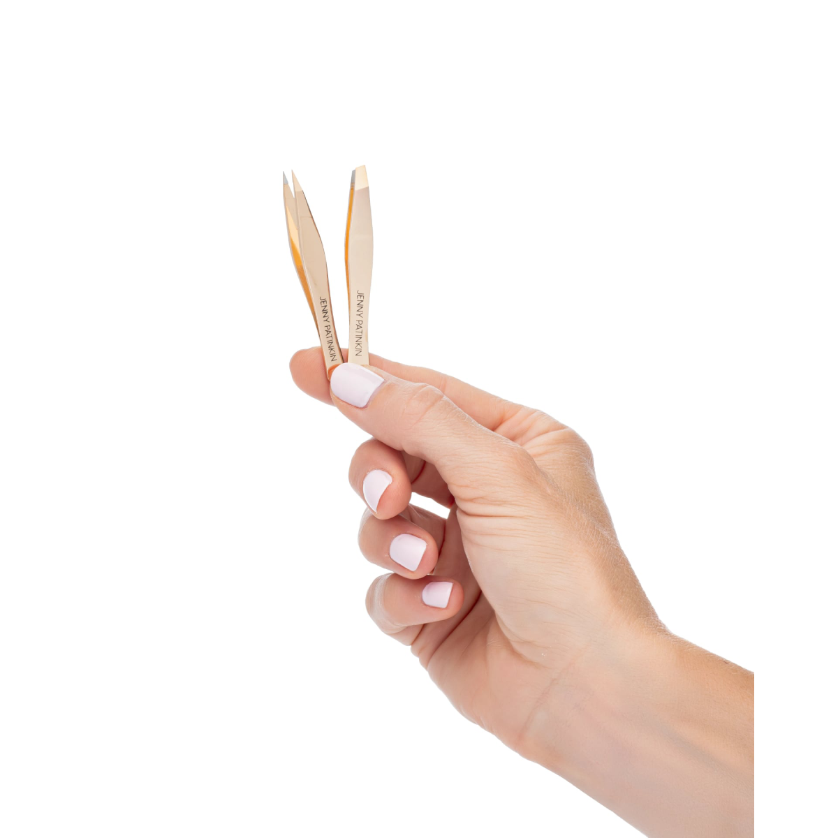 A hand with pale pink manicured nails holds a pair of small gold metal nail tools, likely cuticle pushers or nail emery boards, against a solid white background.