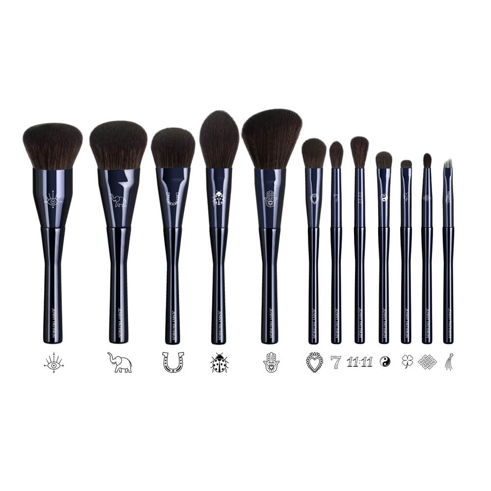 Twelve deep navy makeup brushes from The Superstition Set showing laser-engraved good-luck symbols on each ferrule