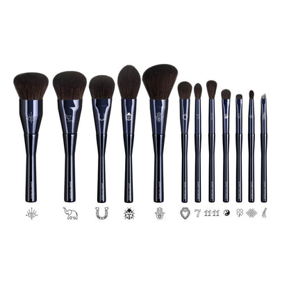 Twelve deep navy makeup brushes from The Superstition Set showing laser-engraved good-luck symbols on each ferrule